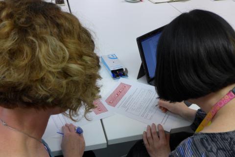 The back of two women's heads viewed over their shoulders as they sign a document.
